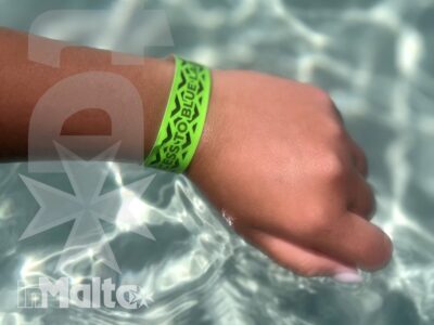 Mano immersa nell'acqua della piscina con braccialetto verde e riflessi luminosi, dettaglio estivo dell'escursione degli studenti a Malta.