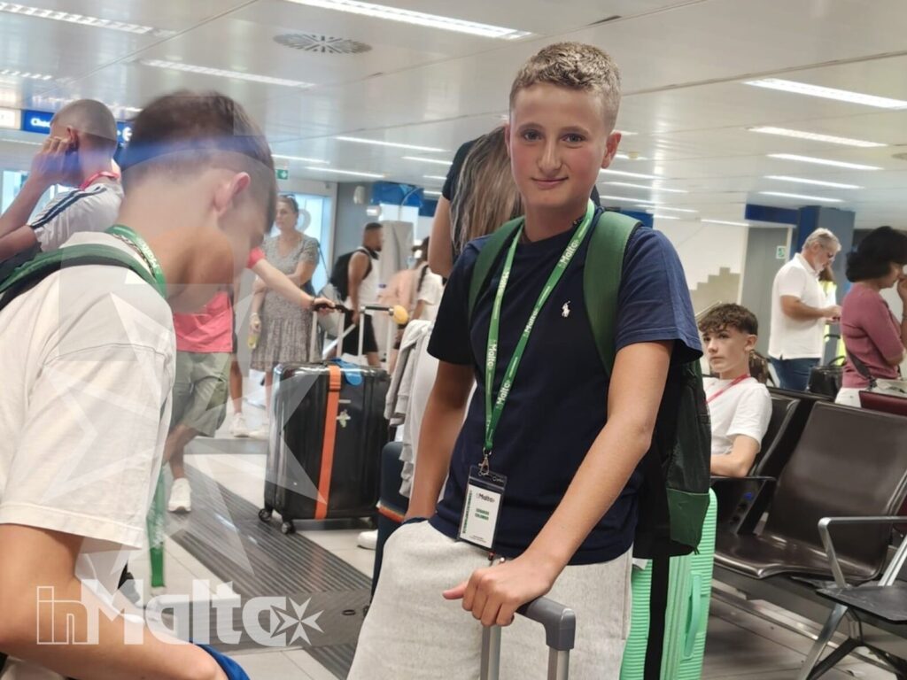 Studenti inMalta con bagagli nell'area partenze aeroportuale Studente con zaino e tesserino resta accanto alla valigia mentre un compagno è seduto nell'area partenze, durante il trasferimento per Malta.