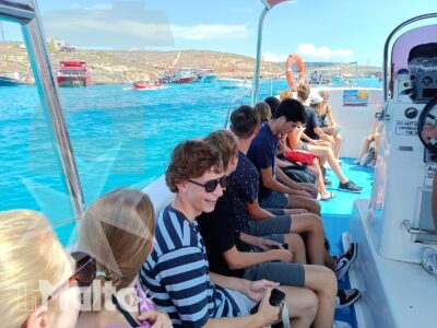 Studenti seduti sul fianco della barca osservano il mare turchese e il porto durante un'escursione a Malta.