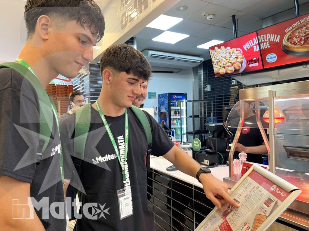 Due studenti con badge e zaini consultano insieme il menu al banco del ristorante durante il viaggio.