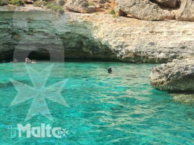 Caletta rocciosa con acqua turchese e bagnanti in lontananza, uno scorcio mediterraneo da vivere durante una giornata di mare a Malta.