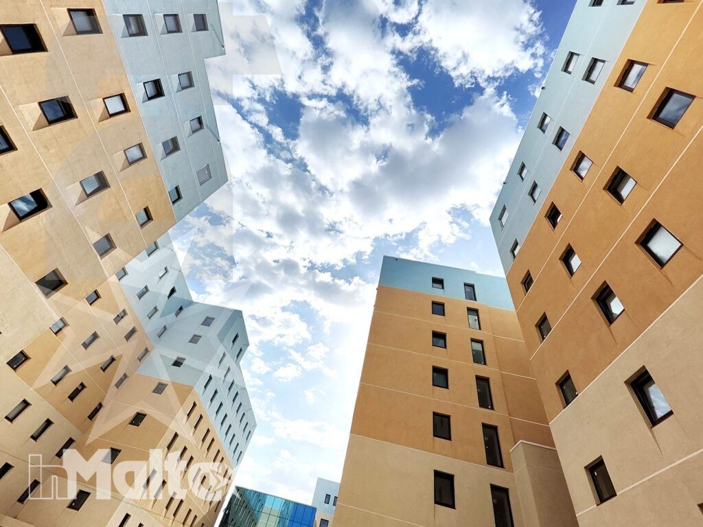 Edifici residenziali dai colori pastello si innalzano intorno a un cortile stretto, incorniciando il cielo del Campus Hub.