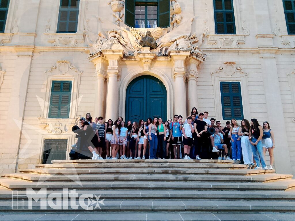 Studenti inMalta davanti a un edificio storico maltese Gruppo internazionale di studenti posa sui gradini davanti a una facciata barocca maltese con grande portone blu.