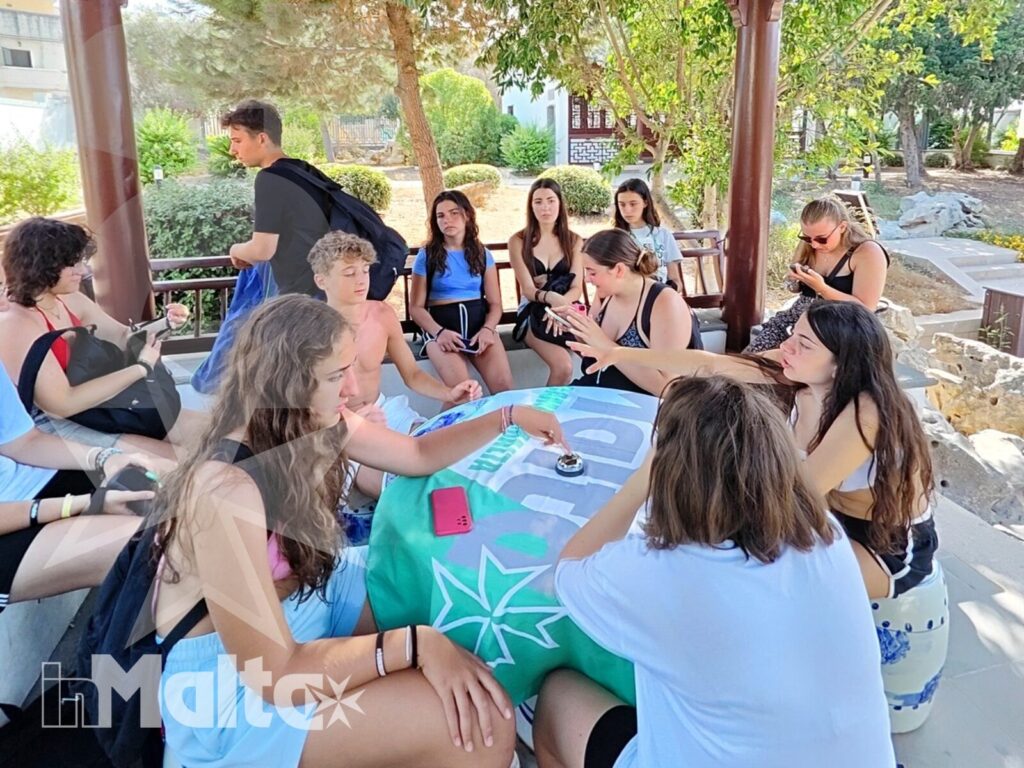 Studenti internazionali conversano attorno a un tavolo in un padiglione decorato affacciato sul verde durante una visita culturale.