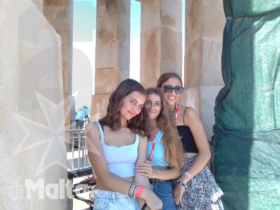 Tre studentesse sorridono tra colonne monumentali in pietra durante una visita culturale a Malta.