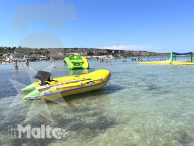 Gommone gonfiabile giallo in primo piano davanti a giochi acquatici e bagnanti, nella baia marina dove si svolgono i Water Games.