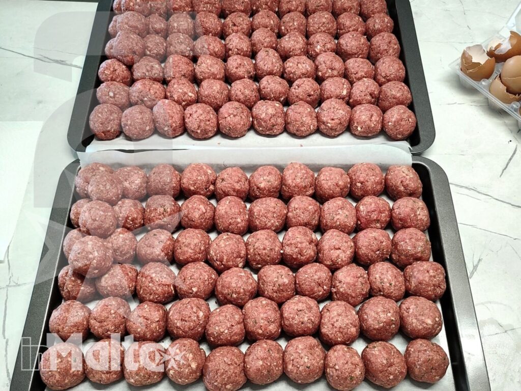 Due vassoi colmi di polpette crude sul piano di lavoro mostrano la preparazione quotidiana della cucina del Campus Hub.