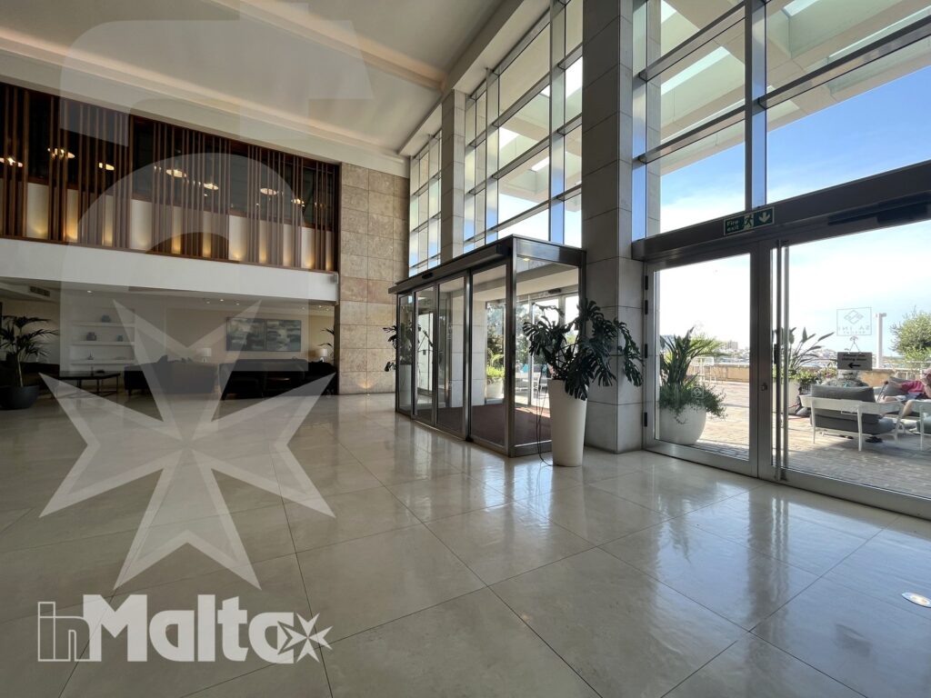 Hall luminosa del Salini Resort con ampie vetrate, ingresso principale, reception e area salotto affacciata sull'esterno.