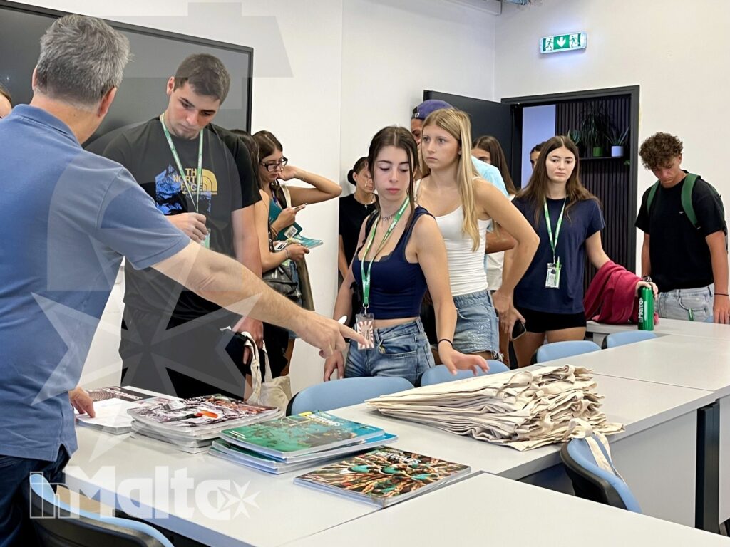Studenti ricevono badge, borse e opuscoli da un tutor presso il punto di accoglienza, all'inizio delle attività formative a Malta.