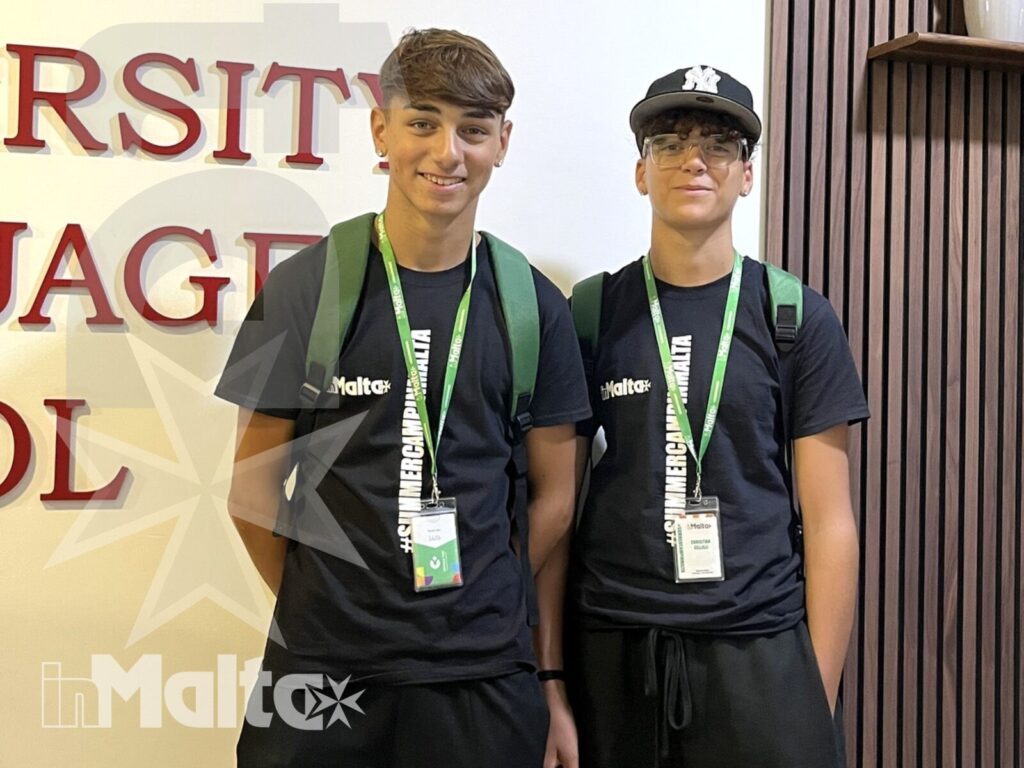 Due giovani partecipanti durante un soggiorno studio a Malta Due studenti adolescenti posano con badge e zaini in un ambiente educativo, parte di un'esperienza di studio a Malta.