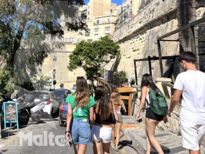 Studenti camminano tra edifici storici in pietra, bouganville e vegetazione mediterranea durante una passeggiata urbana a Malta.