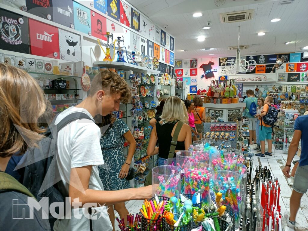 Shopping di souvenir durante una serata a Valletta Studenti e turisti scelgono souvenir colorati in un negozio maltese affollato, tra oggetti locali e prodotti ricordo.