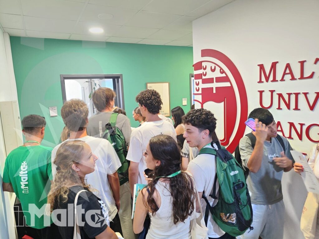Gruppo di studenti con zaini conversa in un corridoio universitario davanti al logo istituzionale, durante un momento di orientamento.