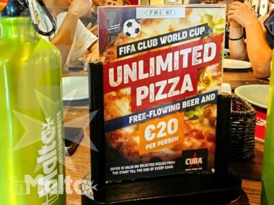 Studenti riuniti attorno al tavolo con pizza e bottiglie riutilizzabili, sotto un murale vivace durante una serata in pizzeria.