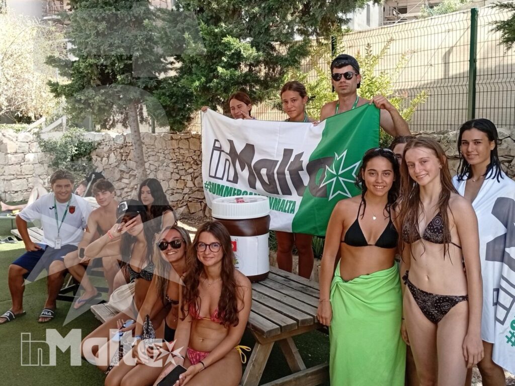Un numeroso gruppo internazionale di studenti si riunisce all'aperto con bandiere e striscioni, esprimendo socialità e spirito di gruppo.