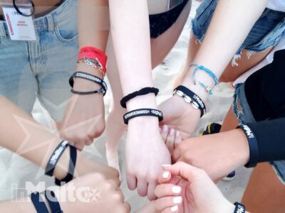Studenti uniscono le mani al centro mostrando braccialetti coordinati, esprimendo collaborazione e appartenenza durante una vacanza studio a Malta.