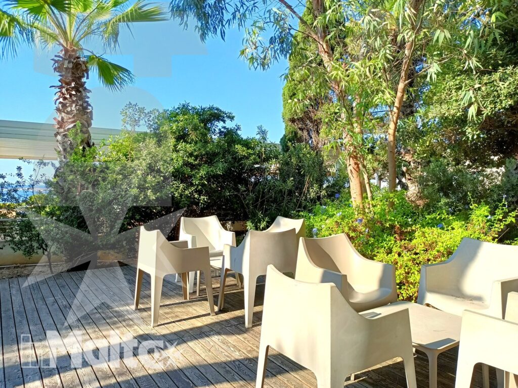 Sedute moderne vuote su una terrazza in legno, circondate da palme e vegetazione mediterranea negli spazi esterni del resort.