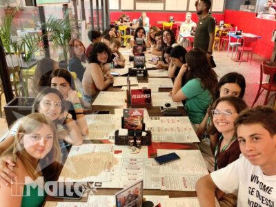 Numerosi studenti siedono a un lungo tavolo apparecchiato, alcuni guardano la fotocamera durante una serata sociale del soggiorno studio.
