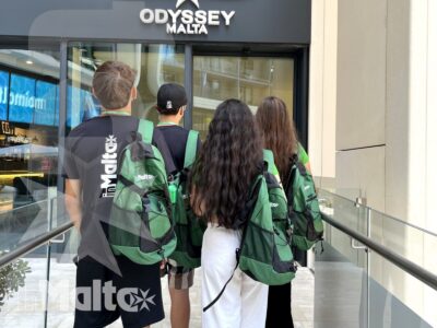Studenti con zaini coordinati camminano verso l'ingresso di Odyssey Malta all'interno di una moderna galleria commerciale.