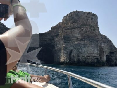 Passeggeri affacciati dalla barca ammirano una grande scogliera sul mare turchese durante un'escursione a Malta