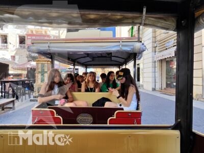 Gruppo di studentesse viaggia su un trenino turistico durante una visita guidata tra le strade urbane maltesi.