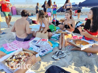Gruppo internazionale di studenti mangia pizza e conversa seduto sulla sabbia, in un momento conviviale organizzato da inMalta.