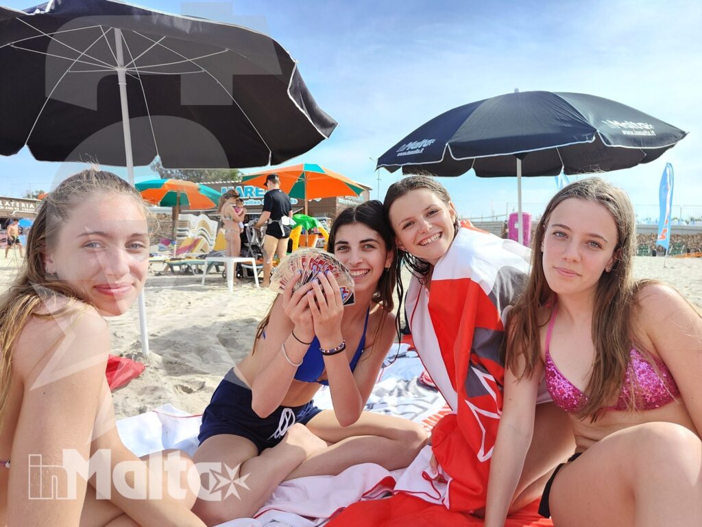 Studentesse inMalta sulla spiaggia di Golden Bay Quattro studentesse sorridono sedute su teli da mare sotto gli ombrelloni durante una giornata a Golden Bay, Malta.