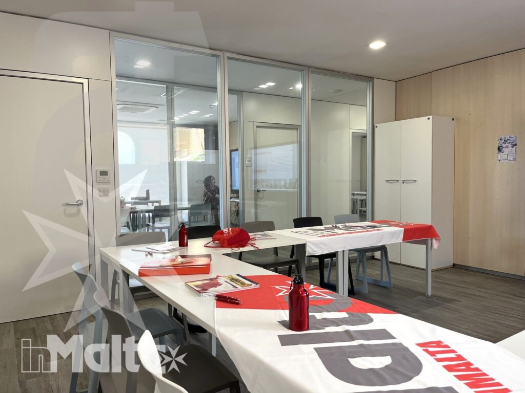 Aula moderna con tavoli a ferro di cavallo, bottiglie e materiali didattici, preparata per accogliere partecipanti a un corso.
