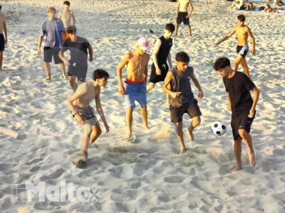 Studenti giocano a calcio sulla sabbia in un momento dinamico e conviviale del loro soggiorno studio al mare.