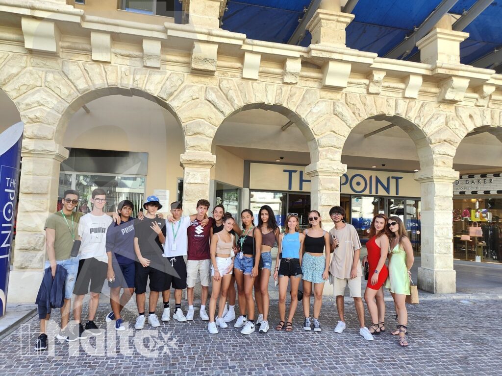 Studenti internazionali posano davanti ai negozi sotto portici in pietra chiara, durante un'uscita diurna a Sliema.
