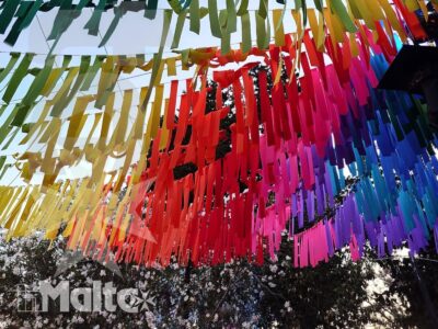 Nastri multicolori sospesi attraversano una strada e incorniciano il cielo, creando una vivace decorazione urbana festiva.