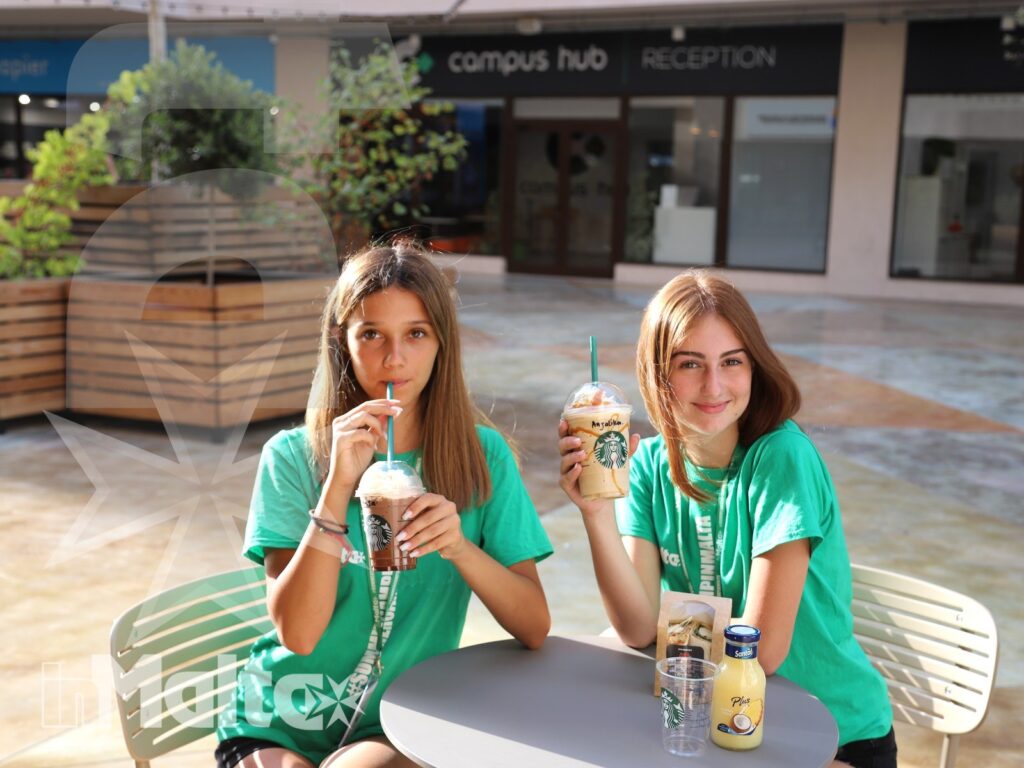 Due studentesse sorridono con bevande fredde all'ingresso del campus, durante una pausa all'aperto del loro soggiorno studio.