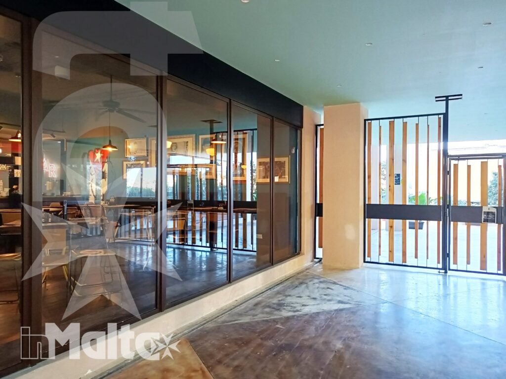 Ingresso moderno con ampie vetrate, porte in legno e sala ristorante visibile, ambiente comune per partecipanti a un soggiorno studio.