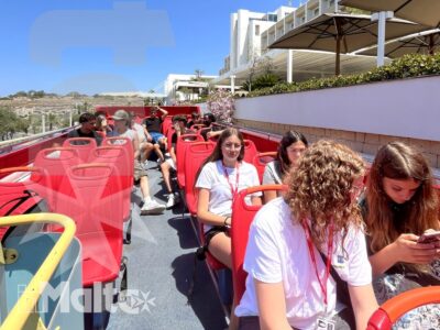 Gruppo di studenti seduti sui vivaci sedili rossi dell'autobus scoperto durante un tour panoramico in una giornata soleggiata.