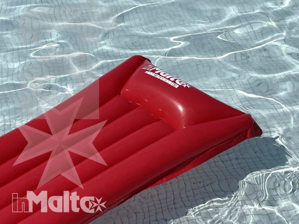Materassino rosso galleggia nella piscina del resort Materassino gonfiabile rosso galleggia nell'acqua limpida della piscina, ripreso dall'alto tra riflessi luminosi e una corsia blu.