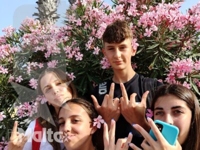 Quattro studenti sorridono davanti a palme e oleandri rosa, immersi nell'atmosfera mediterranea di Malta.