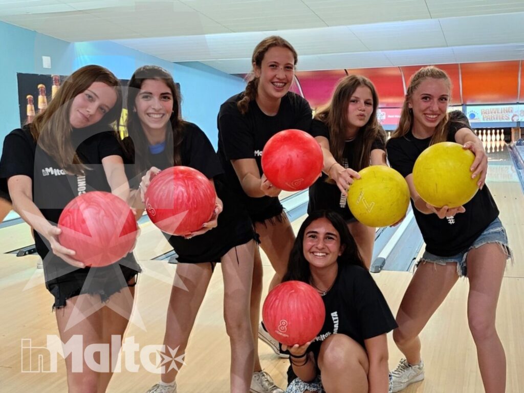 Studentesse sorridenti posano sulla pista da bowling con palle colorate, vivendo un'attività ricreativa di gruppo inMalta.