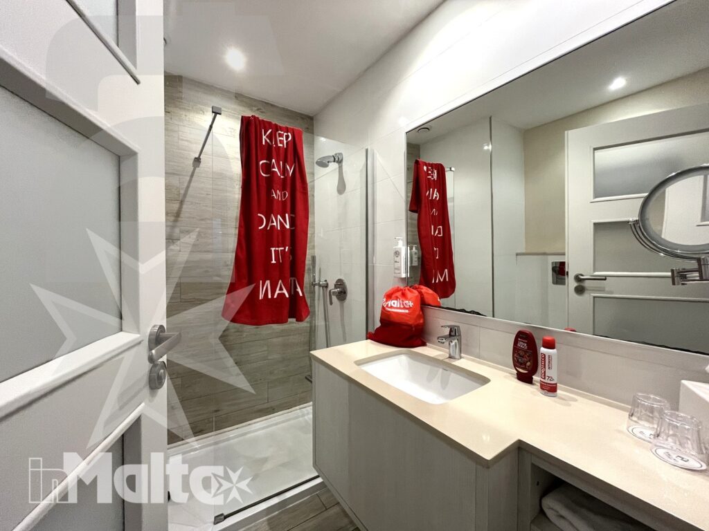Bagno privato moderno con doccia vetrata, lavabo, grande specchio e accessori, a servizio delle camere del resort per giovani ospiti.