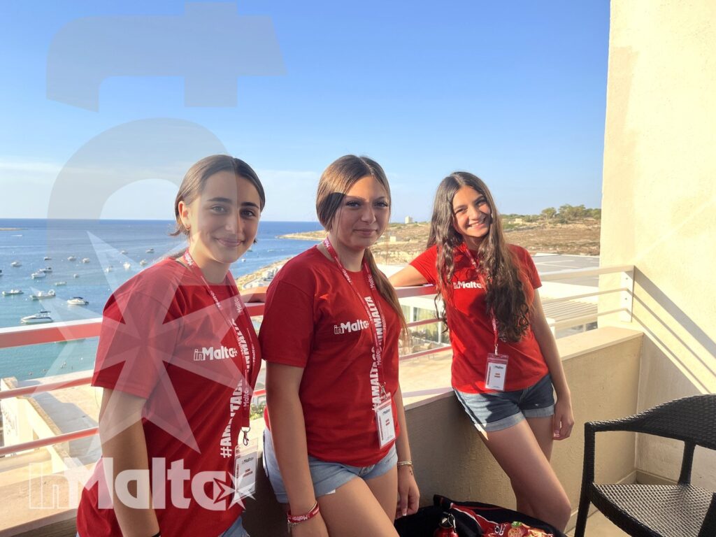 Tre studentesse sorridono sulla terrazza panoramica, con mare, barche e costa maltese sullo sfondo durante il loro soggiorno studio.