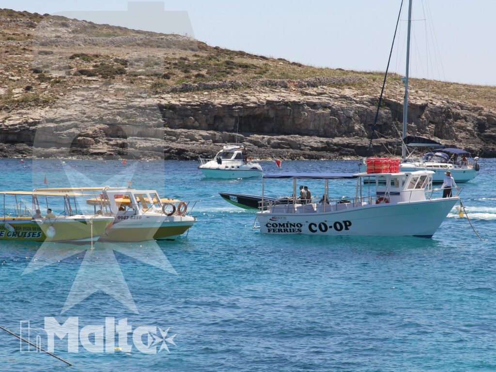 Barche turistiche ancorate in una baia dalle acque turchesi, davanti alla costa rocciosa di Comino.