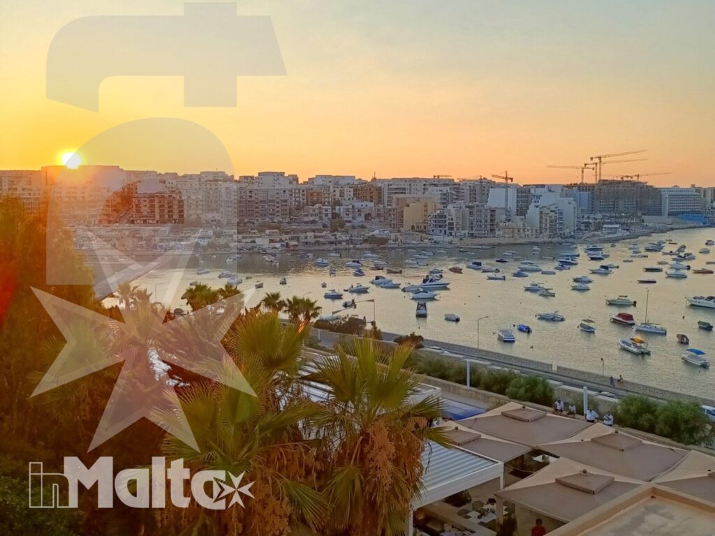 Baia maltese al tramonto, punteggiata di barche e incorniciata da palme e abitazioni sul litorale.