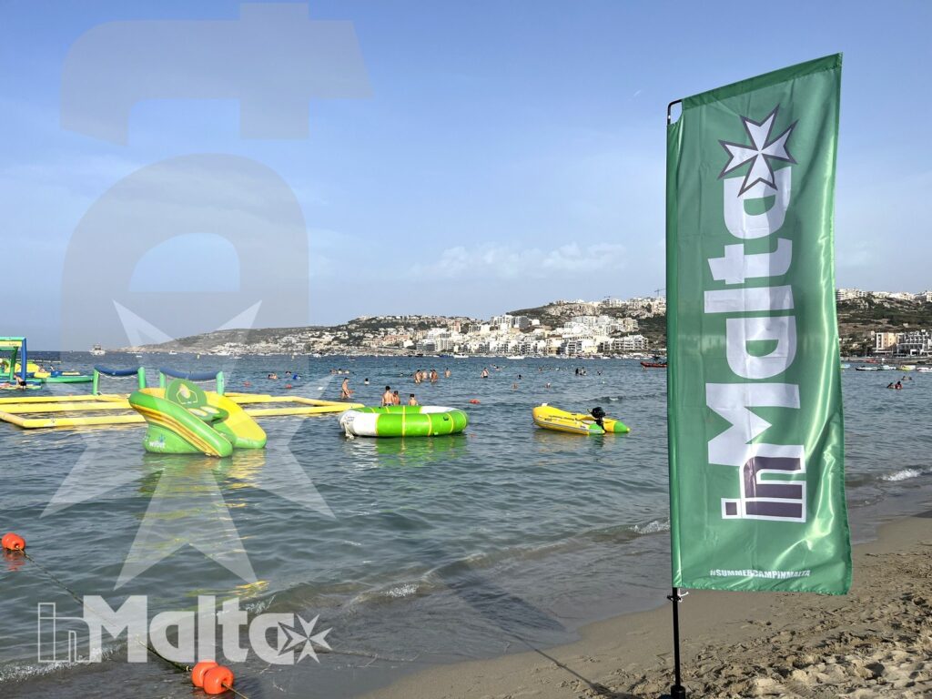 Giochi gonfiabili galleggiano davanti alla costa abitata, mentre la bandiera del centro nautico segnala l'attività ai partecipanti.