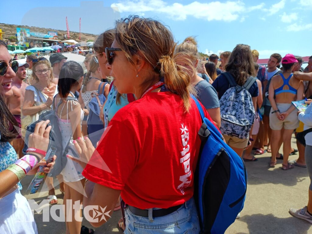 Gruppo di partecipanti durante l'attività alla Blue Lagoon Accompagnatrice con maglietta rossa interagisce con un gruppo di giovani in una vivace area balneare maltese.