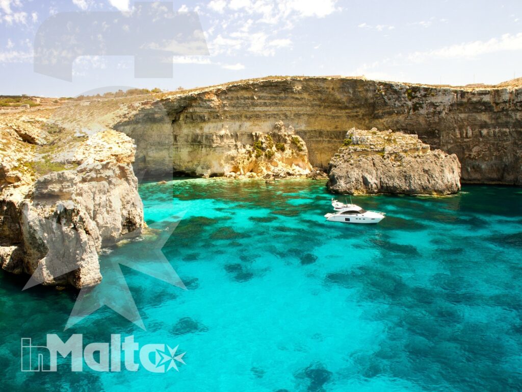 Caletta di Comino con acqua turchese, scogliere calcaree stratificate e una piccola barca al centro della baia.