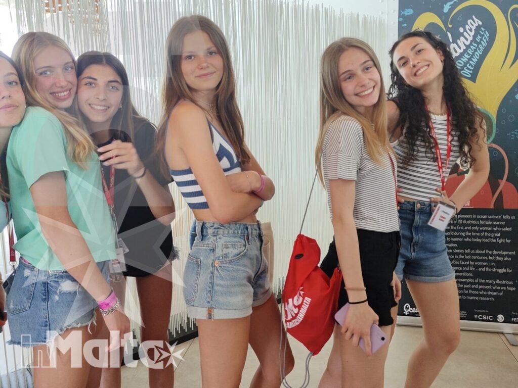 Studentesse in visita culturale durante il soggiorno a Malta Sei studentesse sorridono accanto a un pannello informativo durante una visita culturale in un ambiente museale maltese.