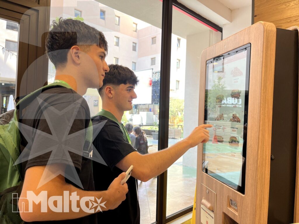 Due studenti leggono e selezionano il menu digitale in un ambiente luminoso e informale.