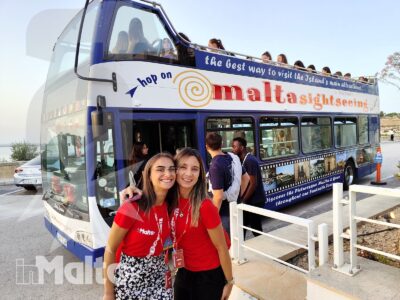 Due studentesse sorridono davanti all'autobus turistico, mentre altri partecipanti attendono di salire per visitare Malta.
