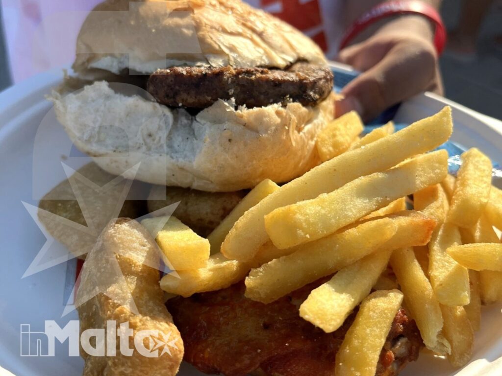 Pasto maltese durante l'attività a Mellieha Bay Primo piano di panino maltese con carne fritta e patatine, servito durante una pausa gastronomica sulla spiaggia di Mellieha Bay.