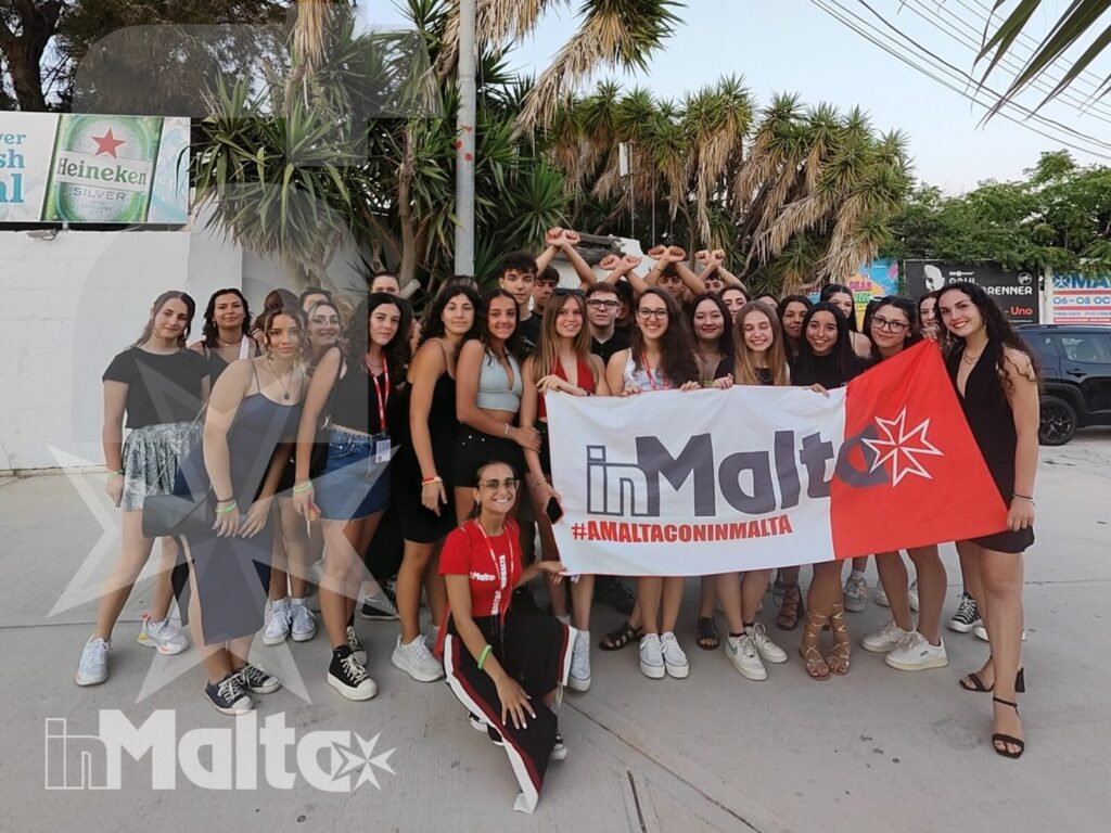Studenti inMalta posano all'aperto con bandiera maltese Gruppo internazionale di studenti posa all'aperto tra palme, striscione promozionale e bandiera maltese.