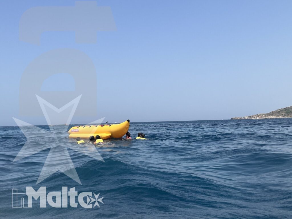 Gommone gonfiabile giallo e partecipanti si muovono sul mare aperto, con una costa bassa visibile all'orizzonte.